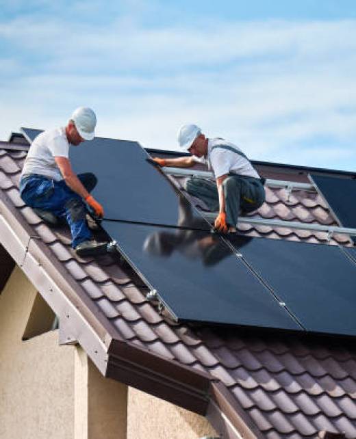 Workers building solar panel system on rooftop of house. Two men installers in helmets installing photovoltaic solar module outdoors. Alternative, green and renewable energy generation concept.